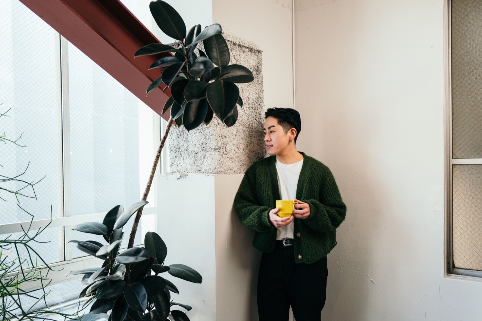 A person pausing with a warm drink beside a large plant