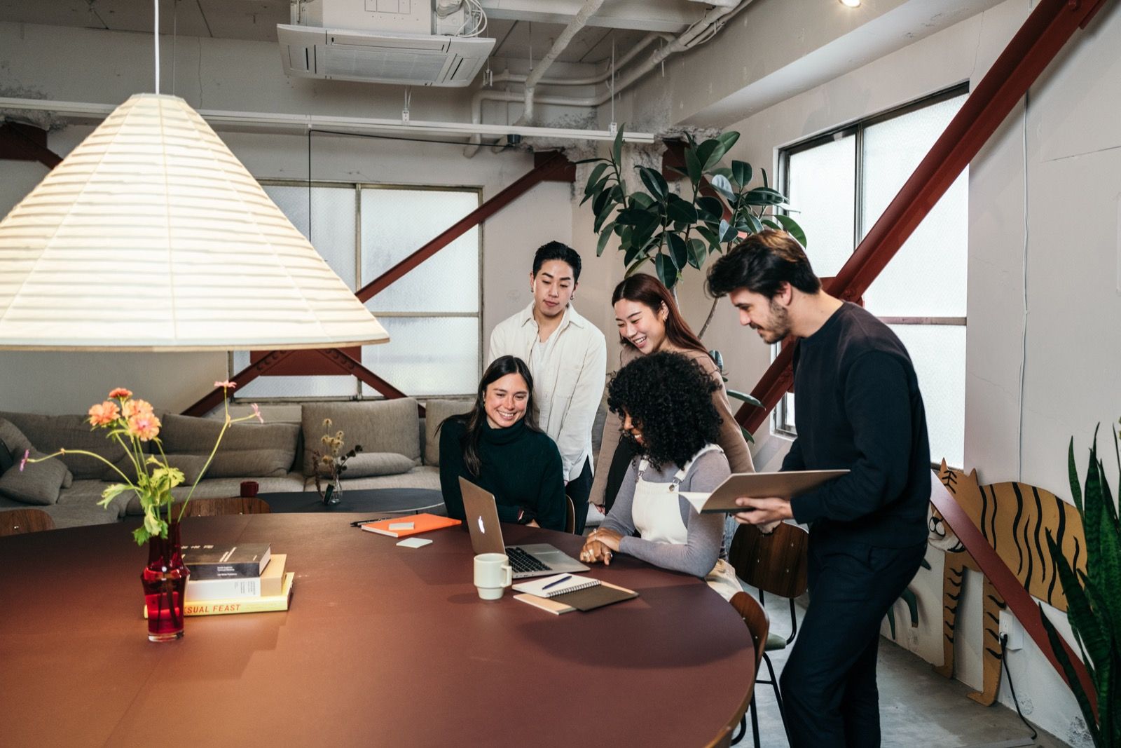 A small, diverse group working together around a table in a warm, plant-filled studio